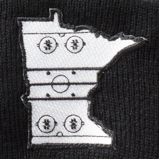 Details of black & charcoal pom hat with patch in the shape of the state outline of Minnesota with the details of a hockey rink on the inside of the state outline. minnesota clothing, minnesota apparel, minnesota accessories, minnesota gifts, minnesota goods, minnesota-themed clothing, minnesota-themed apparel, minnesota-themed gifts, minnesota-themed goods, minnesota pom hats, minnesota pom pom hats