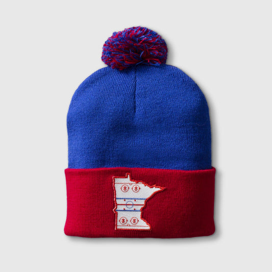 Red & royal pom hat with patch in the shape of the state outline of Minnesota with the details of a hockey rink on the inside of the state outline. minnesota clothing, minnesota apparel, minnesota accessories, minnesota gifts, minnesota goods, minnesota-themed clothing, minnesota-themed apparel, minnesota-themed gifts, minnesota-themed goods, minnesota pom hats, minnesota pom pom hats