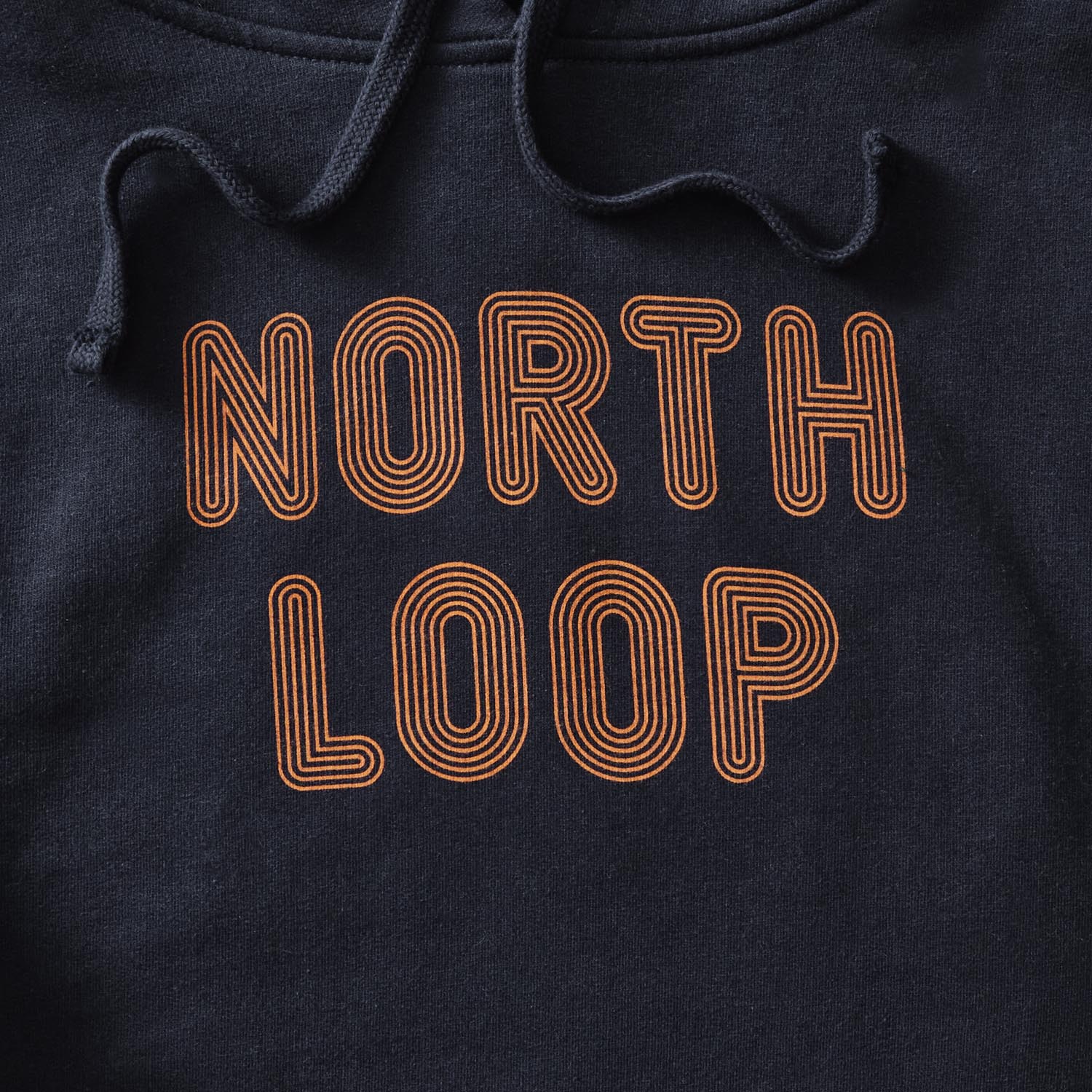 Details of classic navy pullover hoodie with North Loop text in orange with a multi-stroke effect. minnesota clothing, minnesota apparel, minnesota accessories, minnesota gifts, minnesota goods, minnesota-themed clothing, minnesota-themed apparel, minnesota-themed gifts, minnesota-themed goods, twin cities clothing, twin cities apparel, twin cities accessories, minneapolis clothing, minneapolis apparel, twin cities neighborhoods, minneapolis neighborhoods