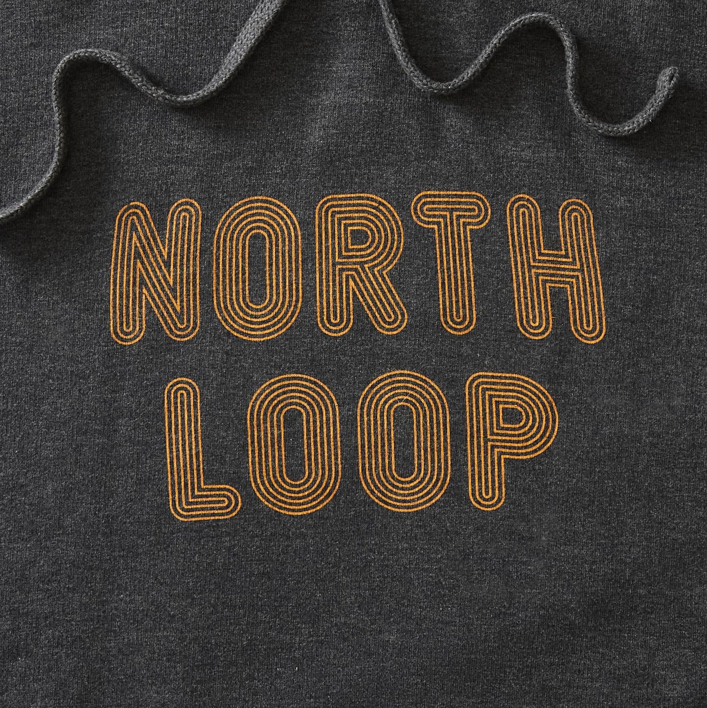 Details of navy heather pullover hoodie with North Loop text in orange with a multi-stroke effect. minnesota clothing, minnesota apparel, minnesota accessories, minnesota gifts, minnesota goods, minnesota-themed clothing, minnesota-themed apparel, minnesota-themed gifts, minnesota-themed goods, twin cities clothing, twin cities apparel, twin cities accessories, minneapolis clothing, minneapolis apparel, twin cities neighborhoods, minneapolis neighborhoods 